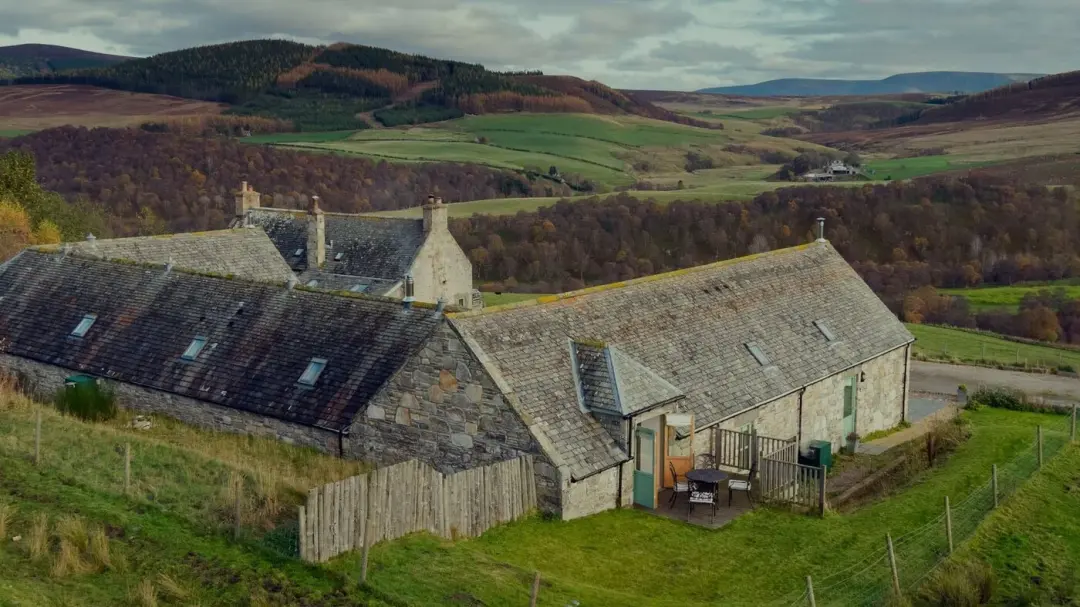 Balneden Steading's stone cottages on the hillside, with the valley and hills beyond