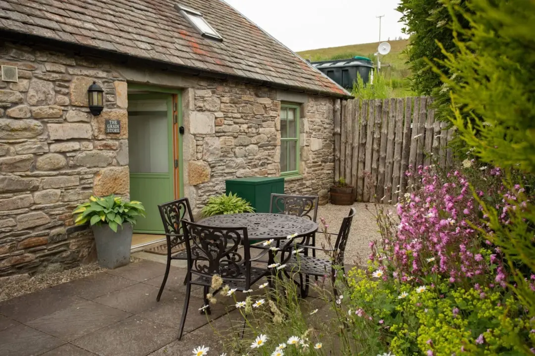 Stone cottage with a green door and a courtyard garden of pink and white flowers