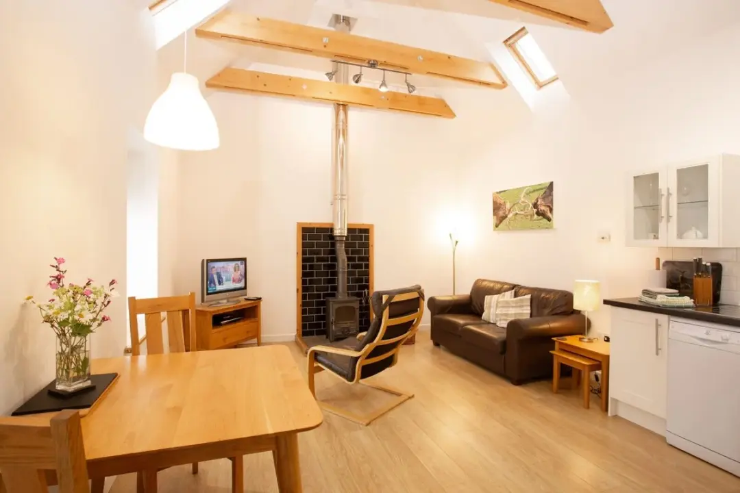 Open-plan living and dining room at The Cattle Shed with a wood-burning stove and beamed ceiling