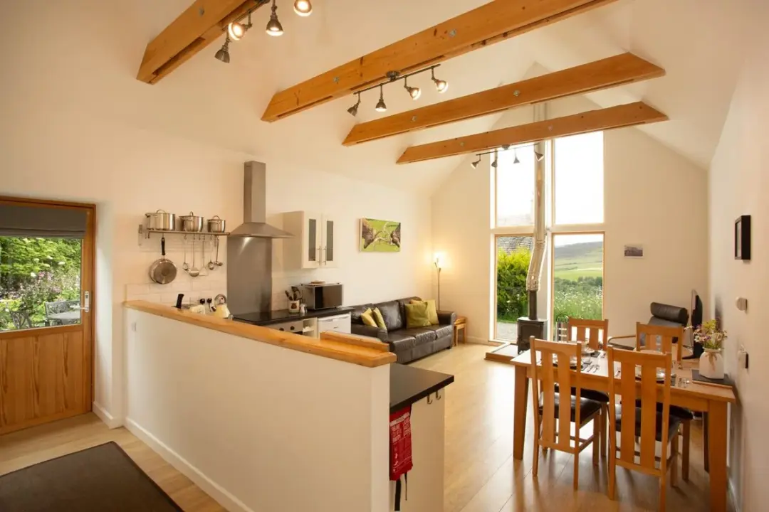 Open-plan kitchen, dining and lounge at The Grain Store with exposed beams and a tall gable window