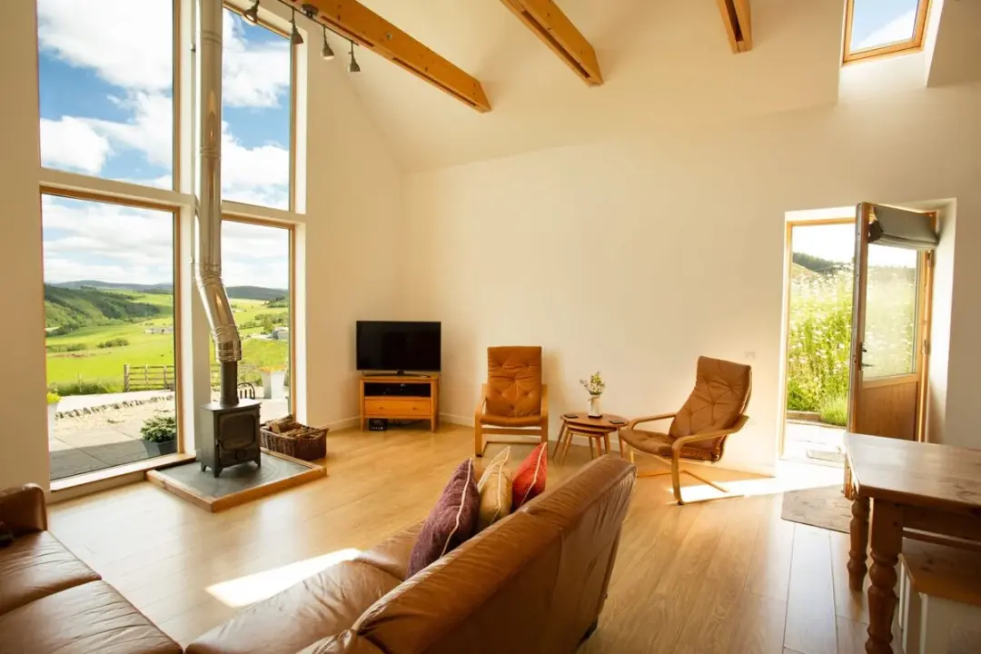 Living room at The Mill with a log-burning stove and tall picture windows looking over green hills
