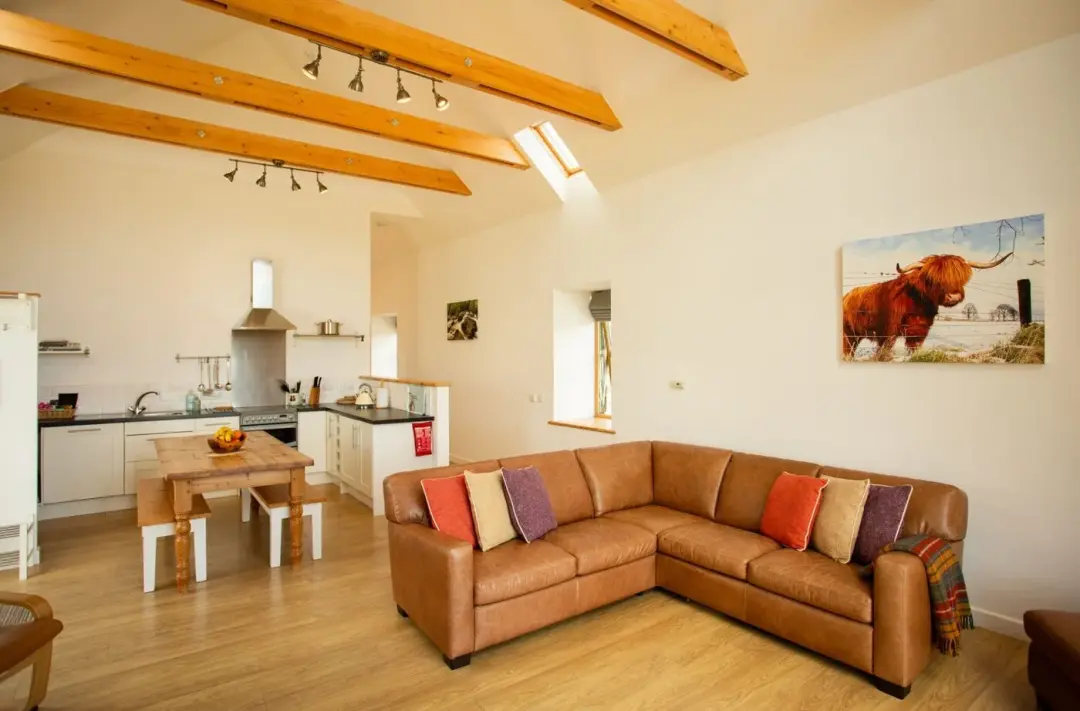 Open-plan kitchen and lounge at The Mill with a leather corner sofa and exposed roof beams